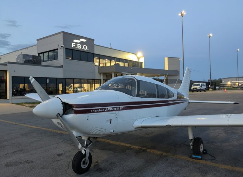 A Piper Cherokee Archer II parked outside an airport FBO at dusk